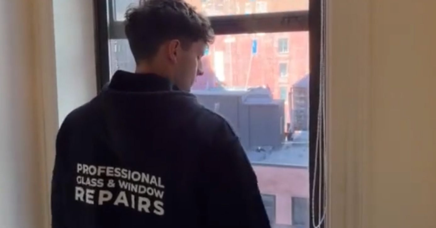 Professional Glass & Window Repairs technician inspecting a window frame from inside a building during a glass repair service